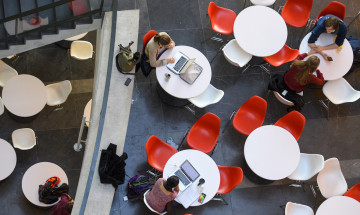 Studenten individueel aan tafels in open ruimte met verschillende devices