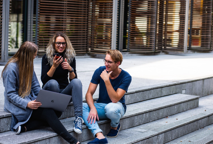 Cybersecurity header - Drie mensen die op een trap zitten en naar een laptop kijken.