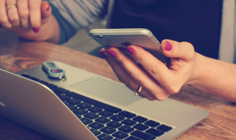 Foto van een vrouw die een mobiele telefoon vasthoudt en achter haar laptop zit.