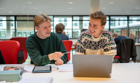 Twee studenten werken op een laptop, de linker wijst naar het scherm