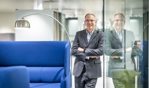 Paul Hillman staat in de gang en leunt tegen een glazen wand