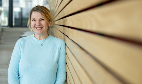 Eveline Crone leunt tegen muur en kijk lachend naar de camera