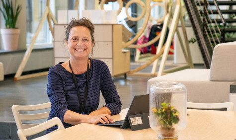 Astrid van Wesenbeeck zit aan tafel met haar laptop en kijk lachend naar de camera