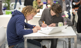 Twee studenten schrijvend aan een tafel met laptop