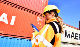 Vrouw in beschermende kleding met tablet bij zeecontainers