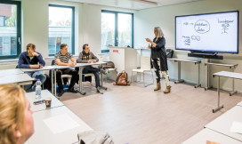 Docente naast een groot beeldscherm voor de klas in U-vorm opstelling