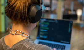Vrouw met koptelefoon gefotografeerd op haar achterhoofd kijkt naar laptop waarvan het scherm onscherp is