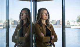 Nolda staat voor een raam met water op de achtergrond en kijkt in de verte