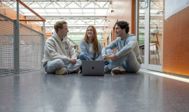 drie studenten zitten op de grond en zijn in gesprek. 