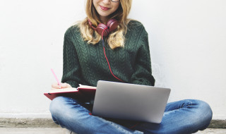 Dame met laptop op schoot en koptelefoon om haar nek die schrijft in een kladblok