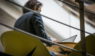 Man achter computer aan tafel op verhoging, foto van verdieping lager genomen