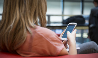 Vrouw van achter gefotografeerd zitten op een bank met een mobiele telefoon in haar hand