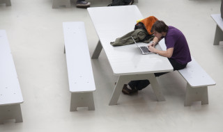Student aan een tafel in een open ruimte met een laptop