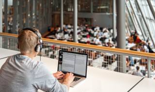 Student achter laptop in bibliotheek vanaf verhoging met koptelefoon