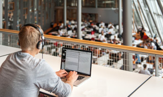 Student achter laptop in bibliotheek vanaf verhoging met koptelefoon