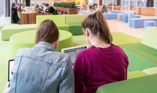 Twee studenten op een groene bank in open ruimte met laptop