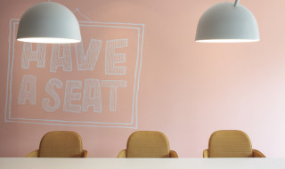 Zicht op een grote tafel met gekleurde stoelen en muur met tekst 'have a seat'