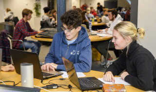 Twee studenten aan tafel achter een laptop in de bibliotheek