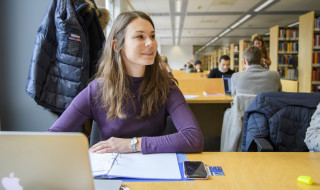 Student aan tafel met computer in bibliotheek