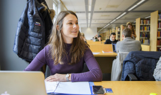 Student aan tafel met computer in bibliotheek