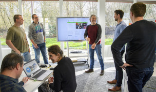 Groep mensen staand voor een groot scherm met elkaar in overleg