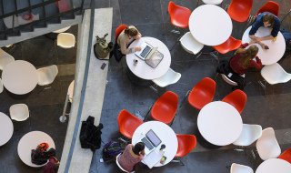 Studenten individueel aan tafels in open ruimte met verschillende devices