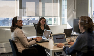 Drie mensen die lachend rond een tafel zitten met laptops
