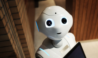 witte robot kijkt je aan met laptop in de hand