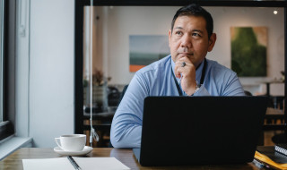 Man met laptop kijkt peinzend naar buiten