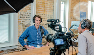 Twee personen aan een tafel met een camera en microfoon