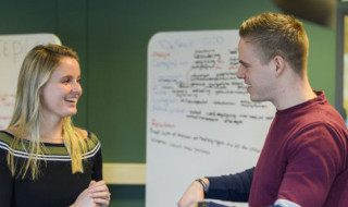 Twee mensen overleggen met whiteboards op de achtergrond