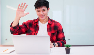 Een student die zit en naar zijn webcam zwaait