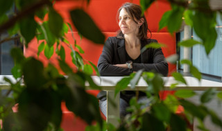 Ana Verbanescu aan tafel, gefotografeerd door de bladeren van een plant heen