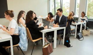 Studenten van de hotelschool netjes gekleed in groepjes aan witte langwerpige tafels
