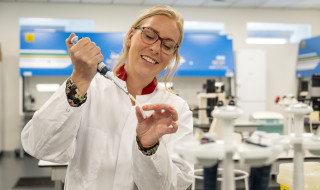 Anna Posthumus vult een reageerbuisje met een pipet. Ze draagt een labjas.