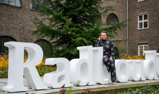 Alexandra van Huffelen sitting on white Radboud letters in the garden of the Berchmanium in Nijmegen