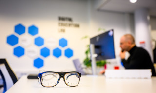 Smart glasses op tafel, Robert Jan Korteland aan het werk op zijn laptop in de achtergrond