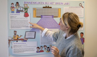 Eveline Crone wijst een poster aan met de titel binnenkijk bij het brein lab