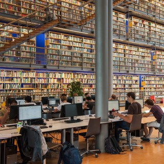 Open bibliotheek met hele hoge boekenwand en werkende studenten