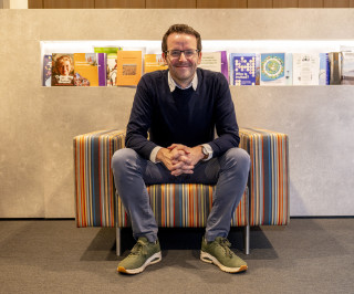 Tom Emery zit en kijkt lachend de camera in 