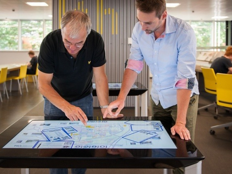 Oudere man met jongere man kijkend naar interactief scherm 