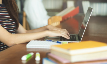 Close-up student achter laptop met schrijfgerei op tafel