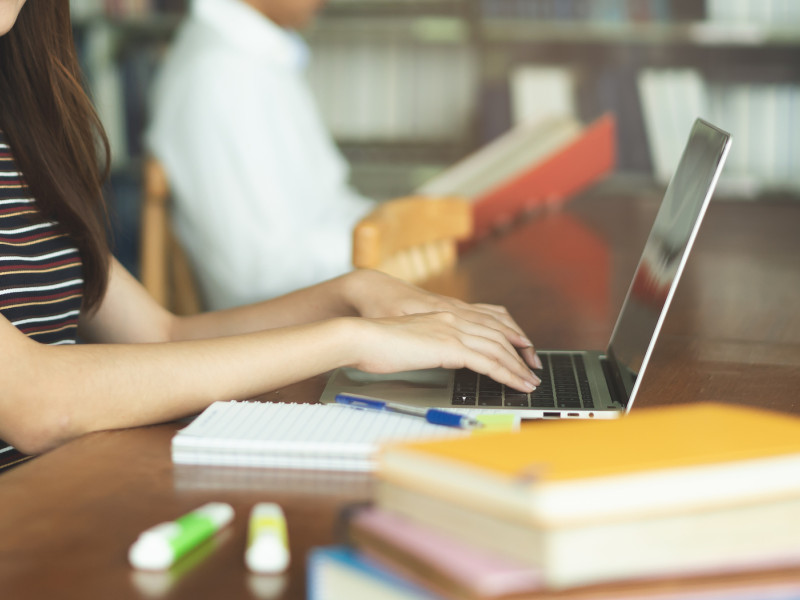 Close-up student achter laptop met schrijfgerei op tafel