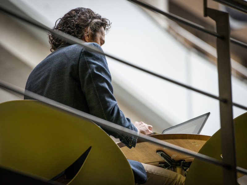 Man achter computer aan tafel op verhoging, foto van verdieping lager genomen