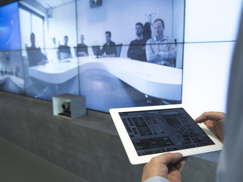 Man met ipad met beeld van conferencecall op de achtergrond