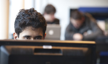 Jongen achter computer te zien waarbij zijn ogen net boven het scherm uitkomen