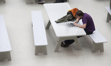 Student aan een tafel in een open ruimte met een laptop