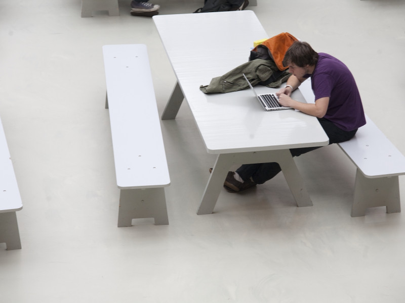 Student aan een tafel in een open ruimte met een laptop