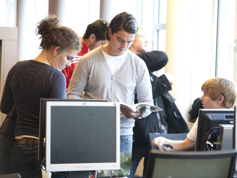 Studenten in open ruimte met computers en handboek