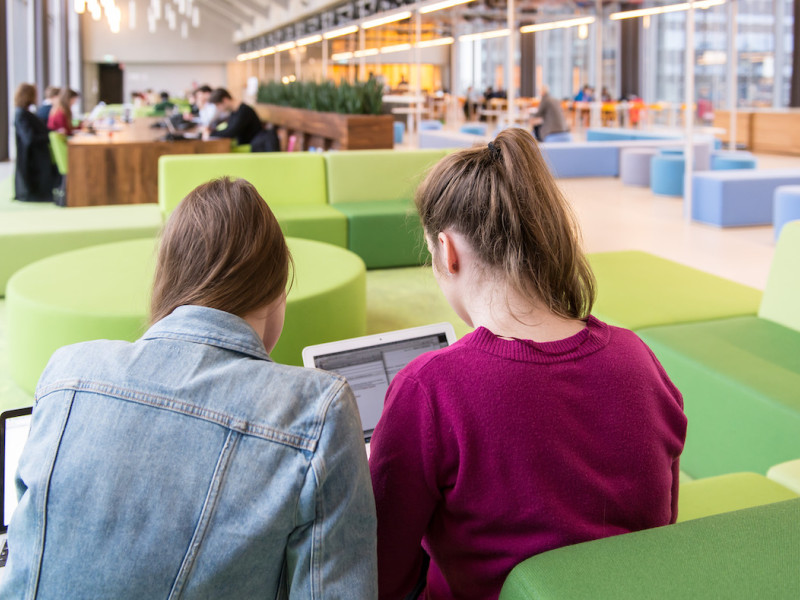 Twee studenten op een groene bank in open ruimte met laptop